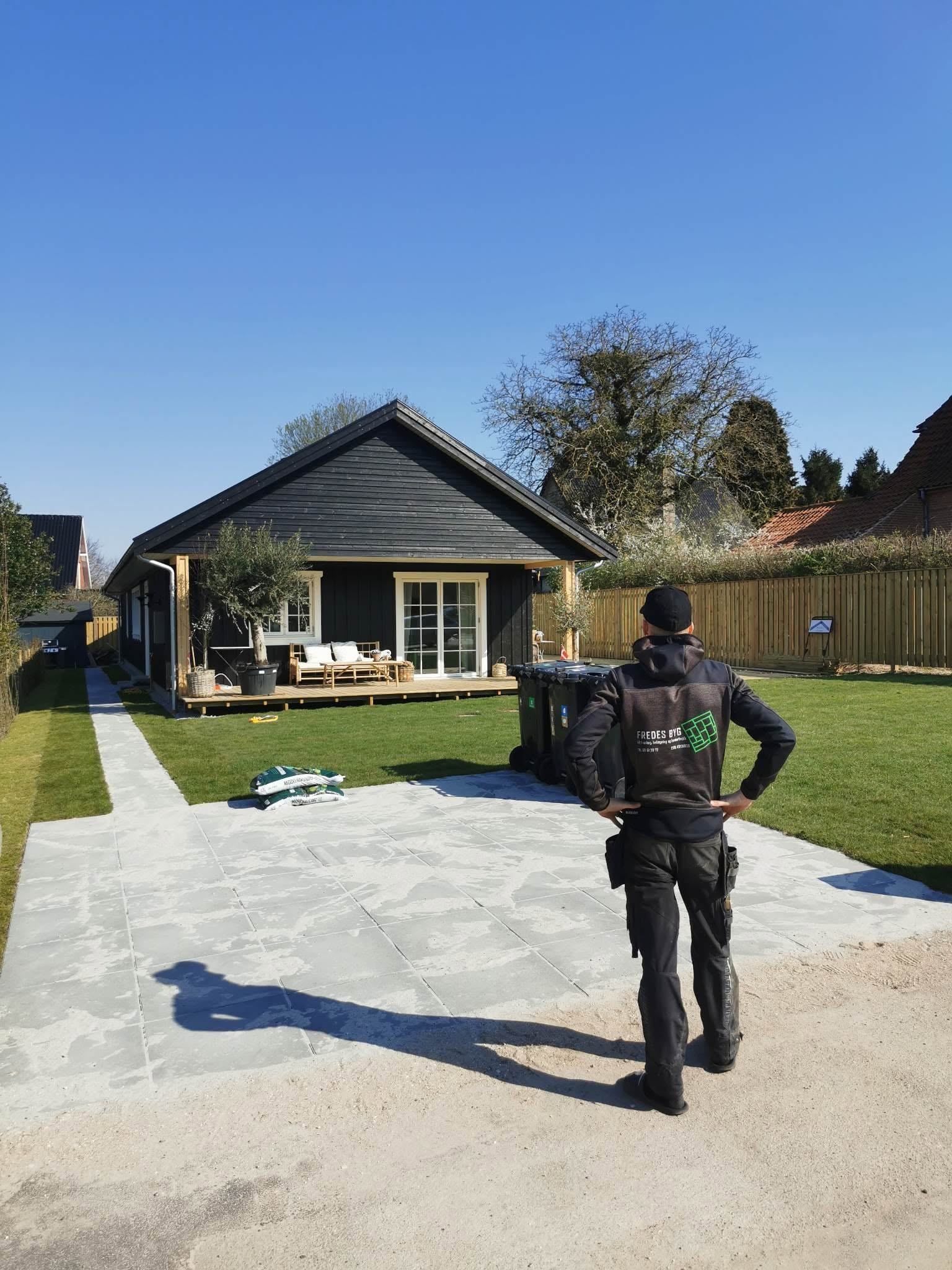 Fredes Byg ved en terrasse med grå fliser foran et mørkt træhus